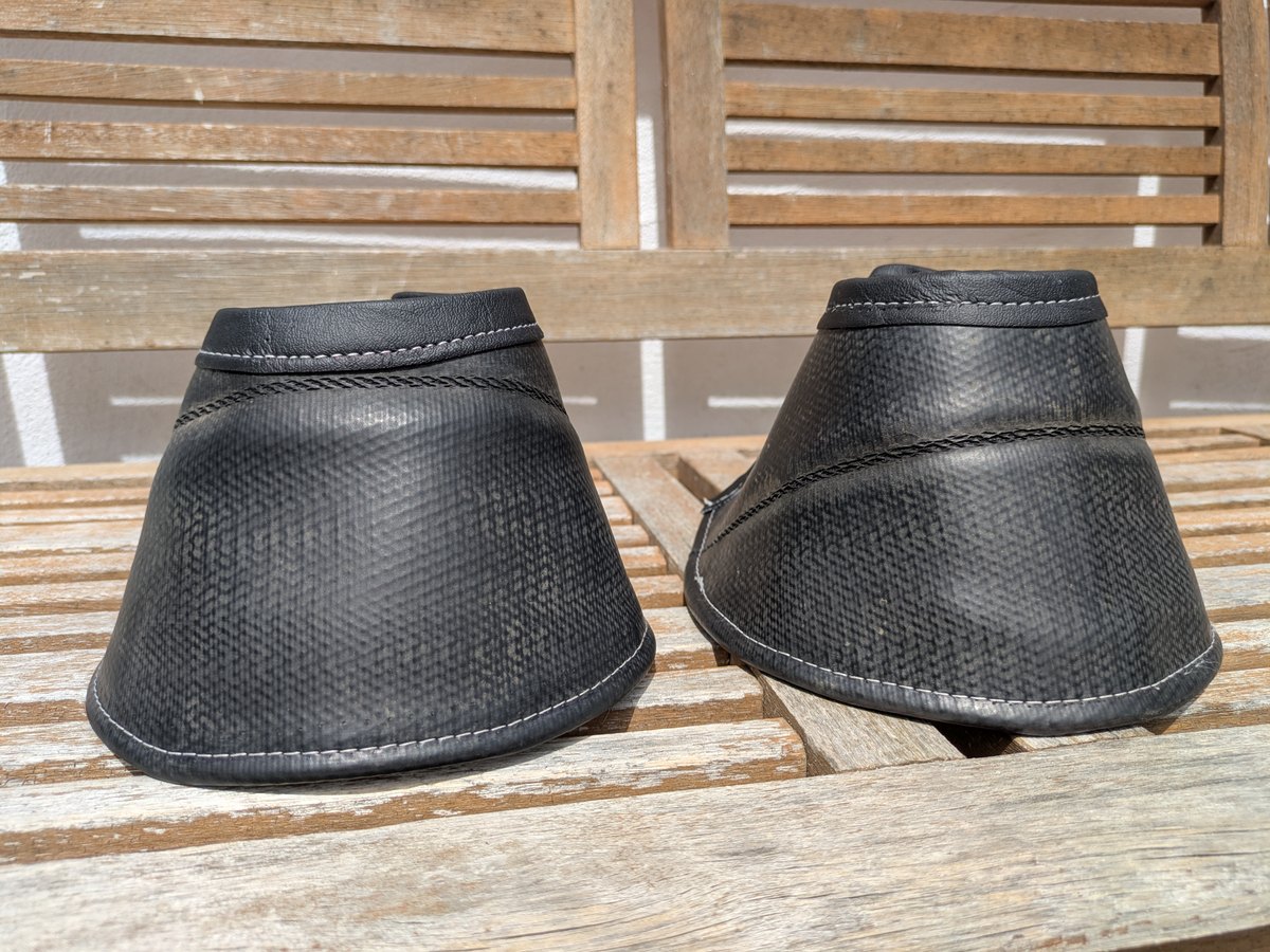 Zwei robuste schwarze Hufglocken aus recyceltem Material auf einer Holzbank