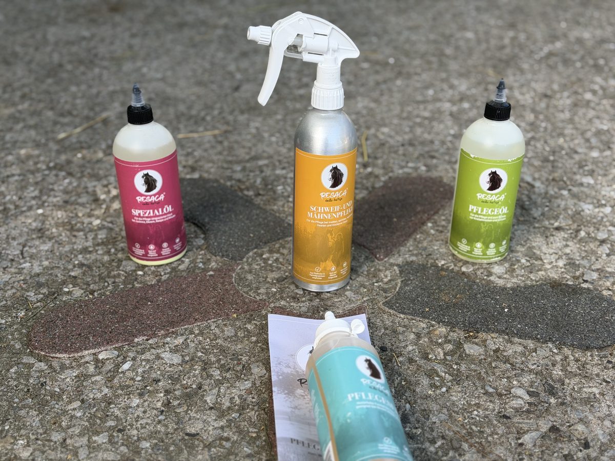 RESACA Pferde-Pflegeprodukte auf dem Stallboden: Spezialöl, Schweif- und Mähnenpflege, Pflegeöl, eine Flasche liegend im Vordergrund