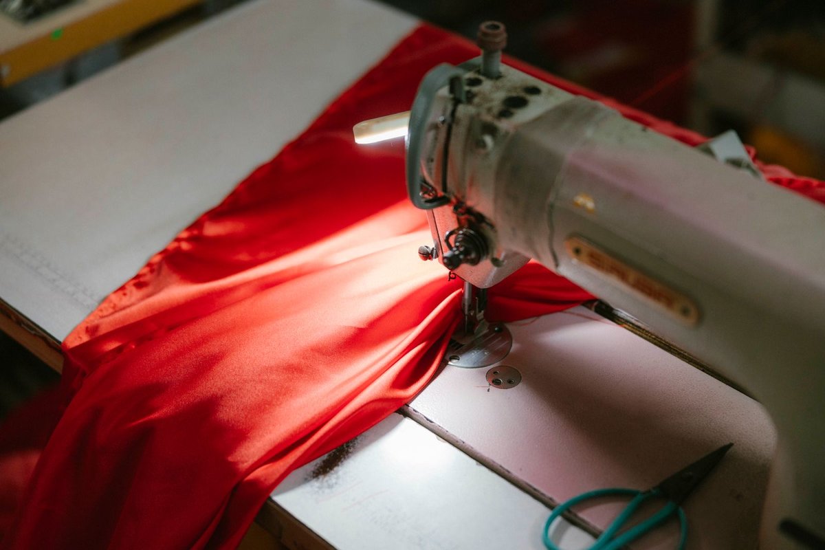 Industrielle Nähmaschine näht roten Stoff, Schere liegt bereit auf dem Arbeitstisch